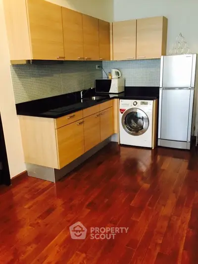 Modern kitchen with wooden cabinets, washing machine, and sleek appliances on polished hardwood floor.