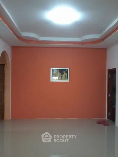 Spacious living room with vibrant orange accent wall and modern ceiling design.