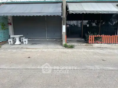 Street view of commercial property with closed shutters and outdoor seating area.