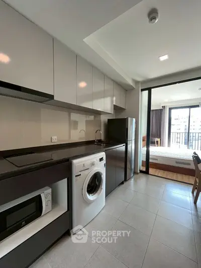 Modern kitchen with sleek appliances and open layout leading to a bright bedroom with balcony.