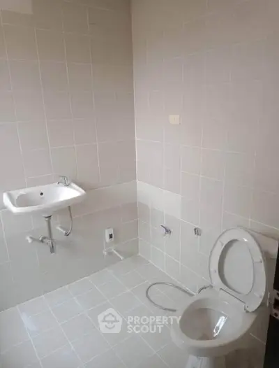 Minimalist bathroom with white tiles and basic fixtures, ideal for modern living.