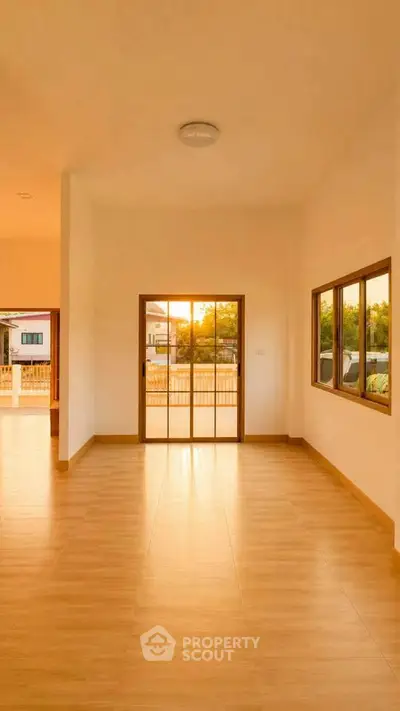 Spacious sunlit living room with large windows and wooden flooring, perfect for modern living.