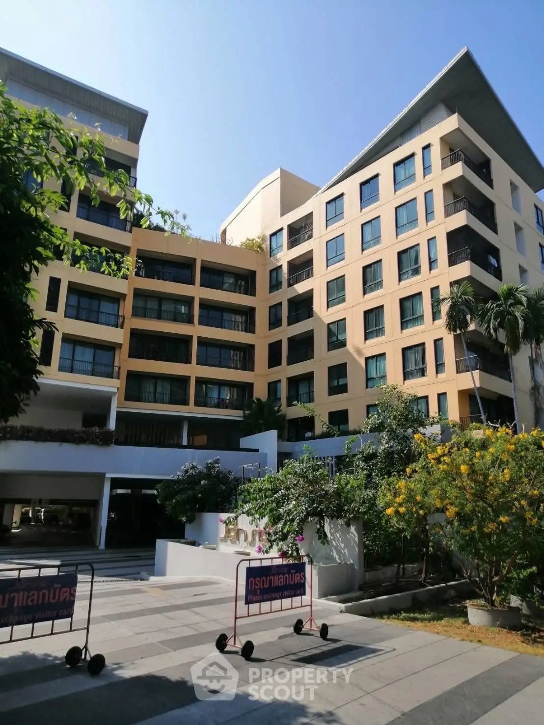 Modern multi-story residential building with lush landscaping and sunny exterior.