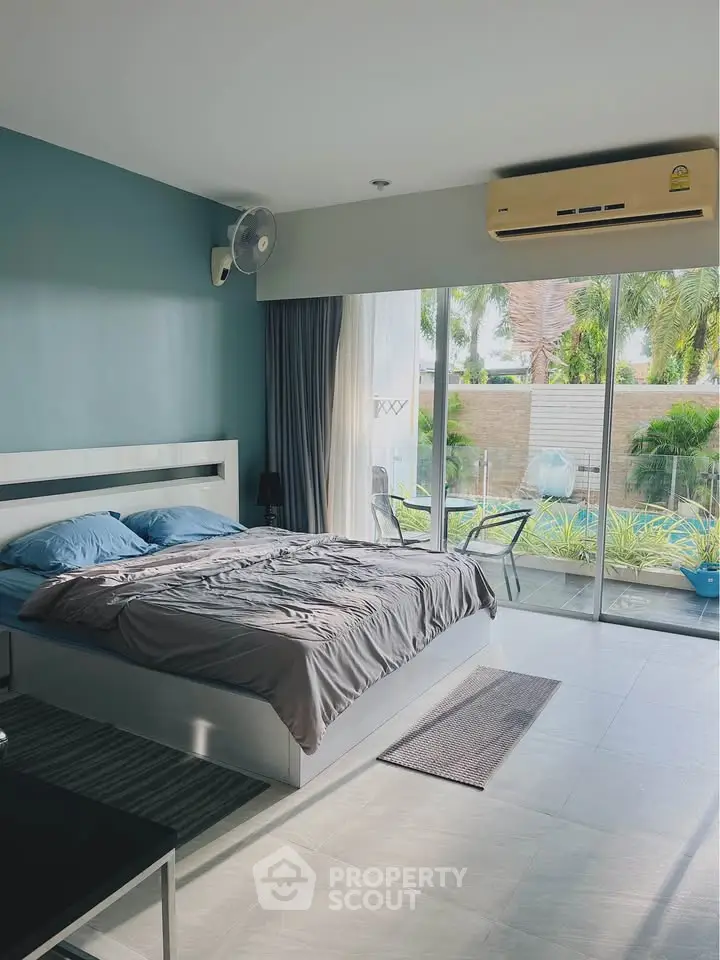 Spacious bedroom with large windows and garden view, featuring modern decor and air conditioning.