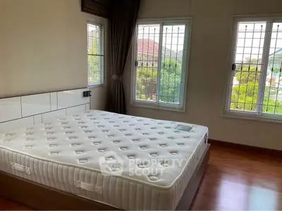 Spacious bedroom with large windows and natural light, featuring a comfortable mattress and wooden flooring.