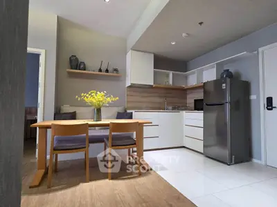Modern kitchen with sleek white cabinets, stainless steel fridge, and cozy dining area with wooden table.