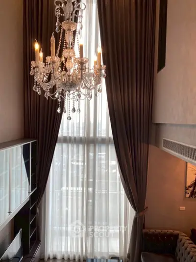 Luxurious high-ceiling living room with elegant chandelier and floor-to-ceiling windows.
