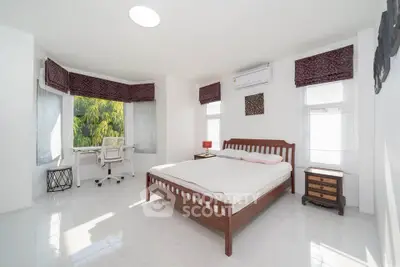 Spacious bedroom with large windows and a study area, featuring modern furniture and natural light.
