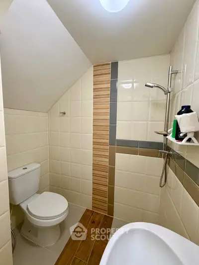 Modern bathroom with sleek design and efficient use of space, featuring a shower and toilet under a sloped ceiling.