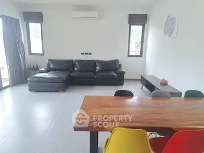 Spacious modern living room with sleek black leather sofa and vibrant dining chairs.