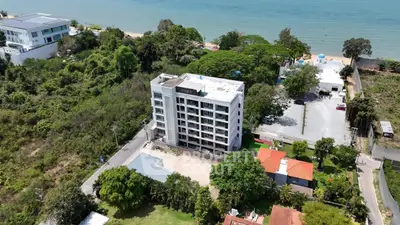 Aerial view of modern beachfront apartment building with lush greenery and ocean backdrop.