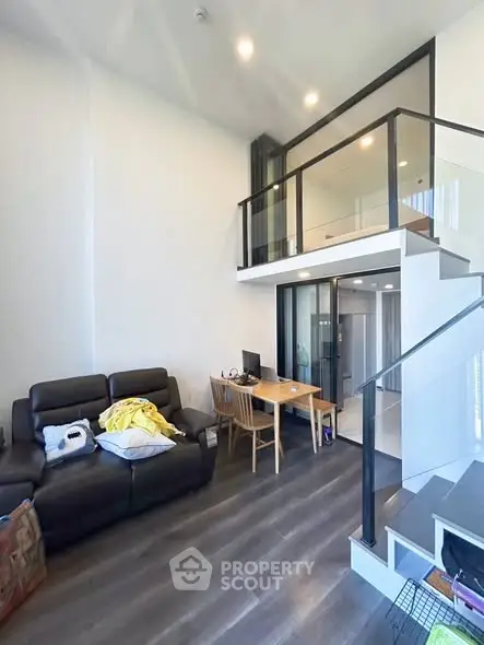 Modern loft-style living room with high ceiling and mezzanine, featuring sleek furniture and stylish decor.