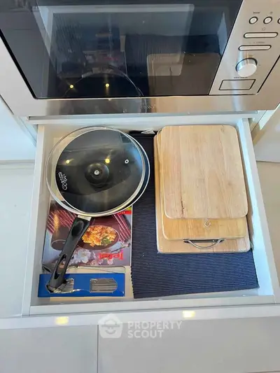 Modern kitchen drawer with cookware and cutting boards in sleek apartment