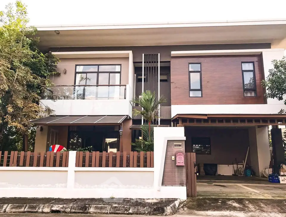Modern two-story house with large windows and a spacious driveway, surrounded by lush greenery.