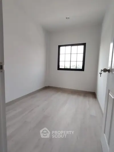 Spacious empty room with large window and wooden flooring, perfect for customization.
