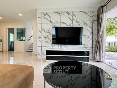 Modern living room with marble accent wall and large TV, open to lush garden view.