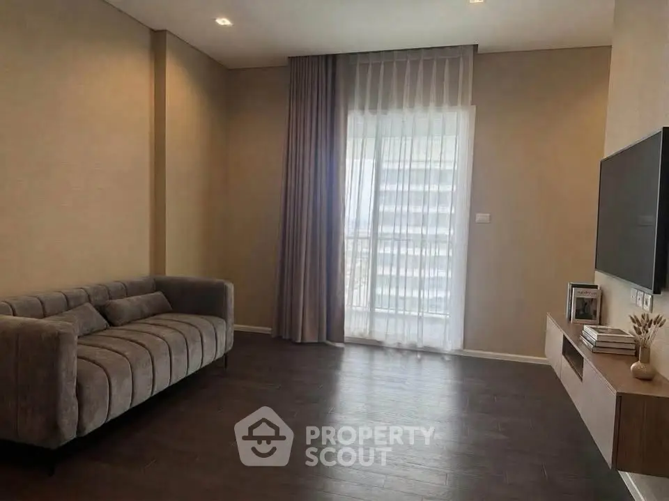 Modern living room with sleek sofa and wall-mounted TV, featuring floor-to-ceiling window with elegant curtains.