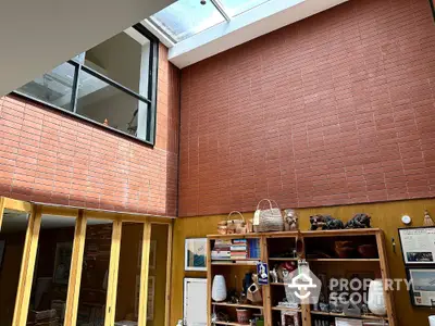 Spacious interior with high ceiling and skylight, featuring a brick wall and wooden shelving.