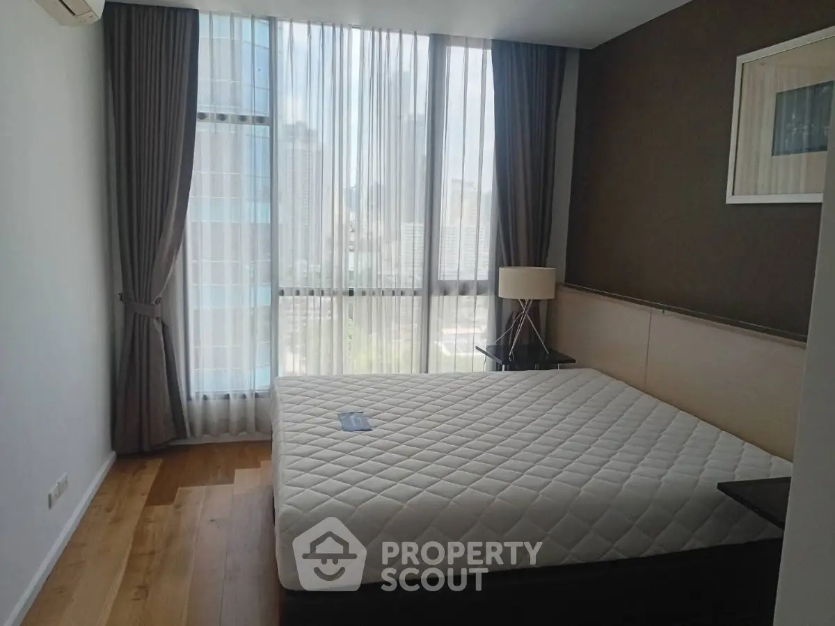 Modern bedroom with large window and city view, featuring a comfortable bed and stylish decor.