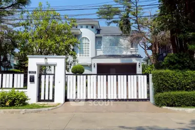 Elegant modern house with gated entrance and lush greenery in a serene neighborhood.
