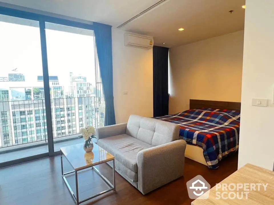 Modern studio apartment with balcony and city view, featuring cozy bed and stylish sofa.