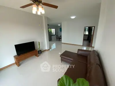 Spacious living room with modern sofa and TV, open layout leading to kitchen.
