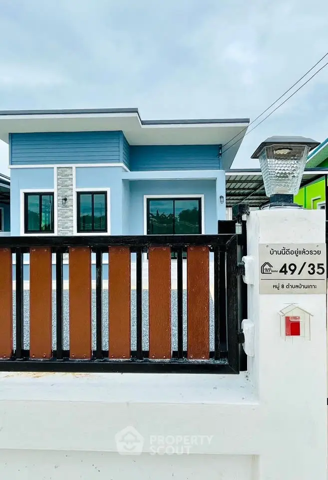 Modern single-story house with blue facade and gated entrance in a serene neighborhood.