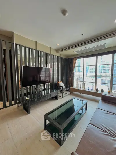 Modern living room with large TV and city view, featuring sleek furniture and ample natural light.