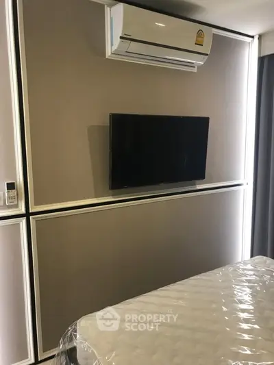 Modern bedroom with wall-mounted TV and air conditioning unit, featuring sleek design and neutral tones.