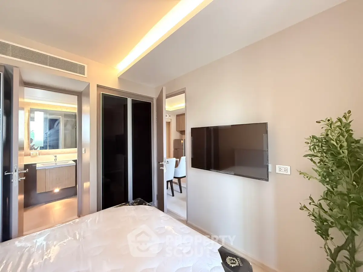 Modern bedroom with sleek design, wall-mounted TV, and ensuite bathroom in luxury apartment.