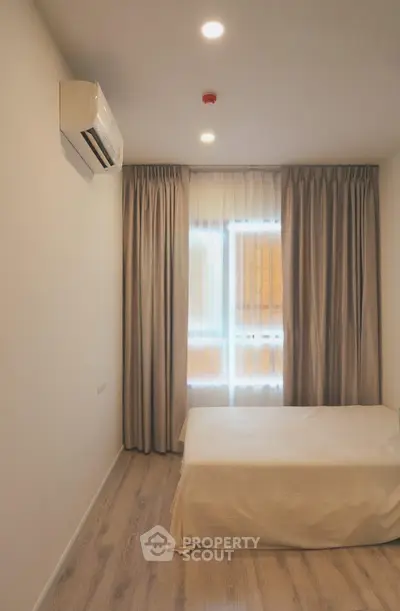 Cozy bedroom with natural light and modern air conditioning unit, featuring elegant curtains and wooden flooring.