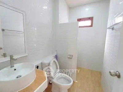 Modern bathroom with white tiles and wooden flooring, featuring a sleek sink and toilet.