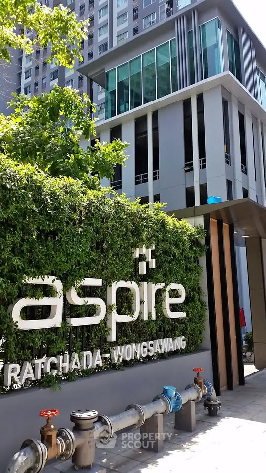 Modern residential building with lush greenery at Aspire Ratchada Wongsawang entrance.