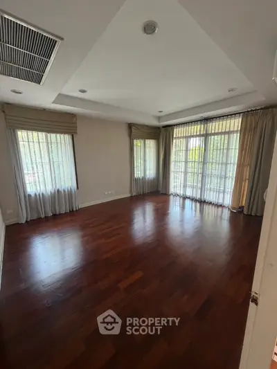 Spacious empty room with hardwood floors and large windows offering natural light.