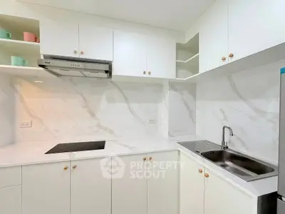 Modern kitchen with sleek white cabinetry and marble countertops, featuring an induction cooktop and stainless steel sink.