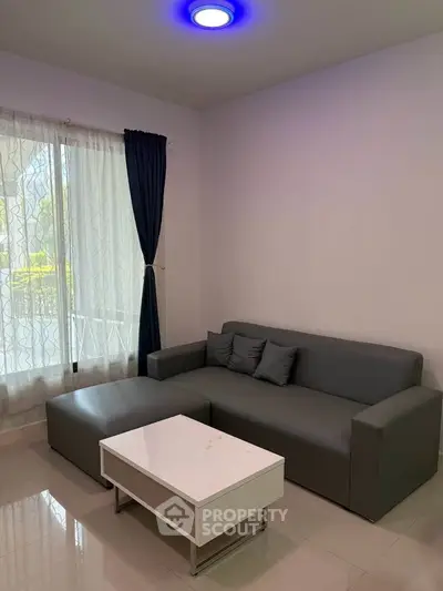 Modern living room with sleek gray sofa and stylish coffee table, featuring elegant curtains and ambient lighting.