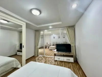 Spacious bedroom with mirrored closet and view into cozy living area, featuring elegant wood flooring.