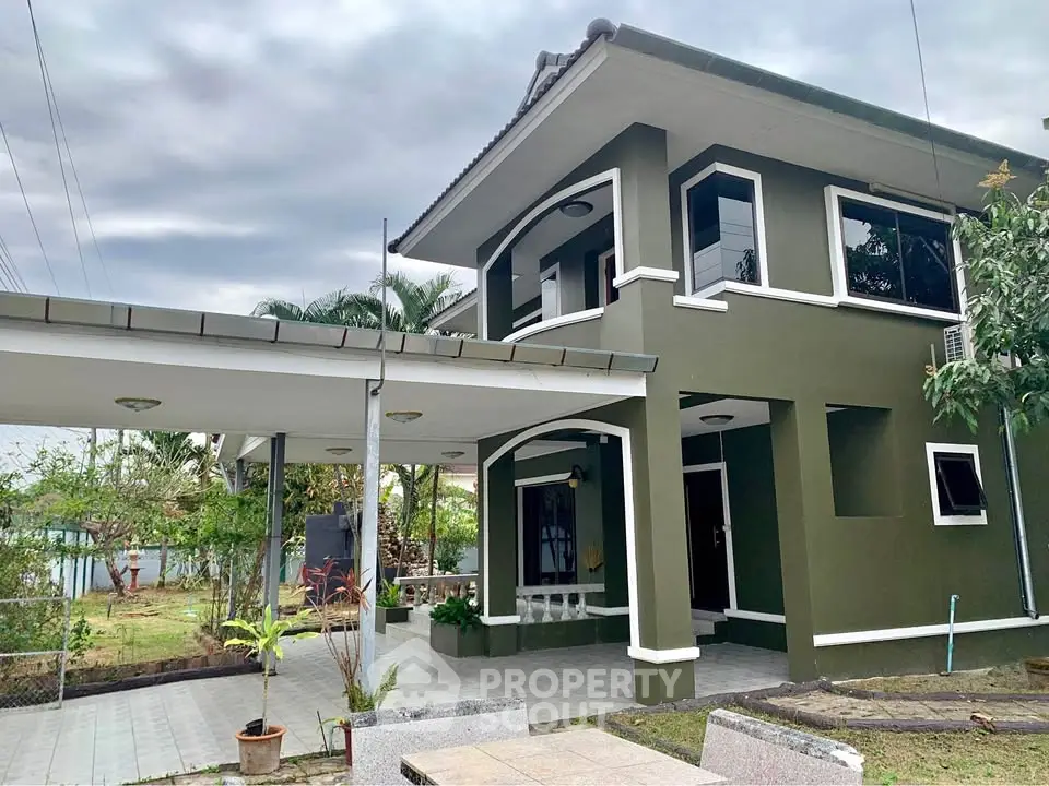 Charming two-story green house with covered carport and lush garden, perfect for family living.