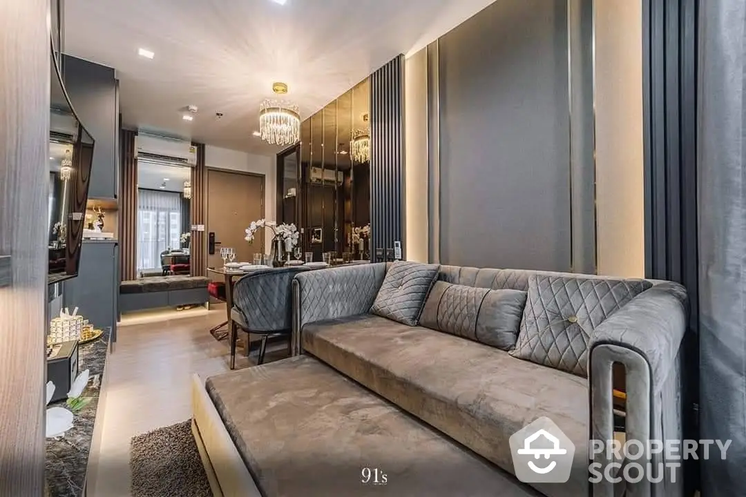 Elegant living room with plush grey sofa, chic chandelier, and a seamless transition to a modern kitchen, perfect for sophisticated urban living.