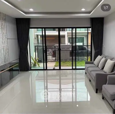 Modern living room with large windows and sleek design overlooking a garden view.