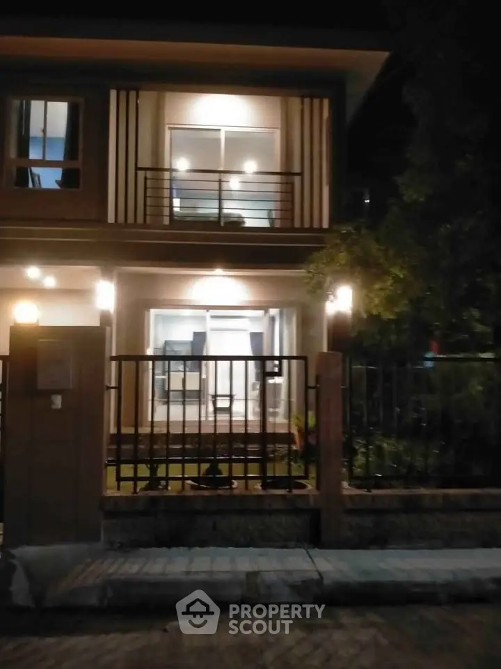 Modern two-story house with illuminated exterior and fenced yard at night.