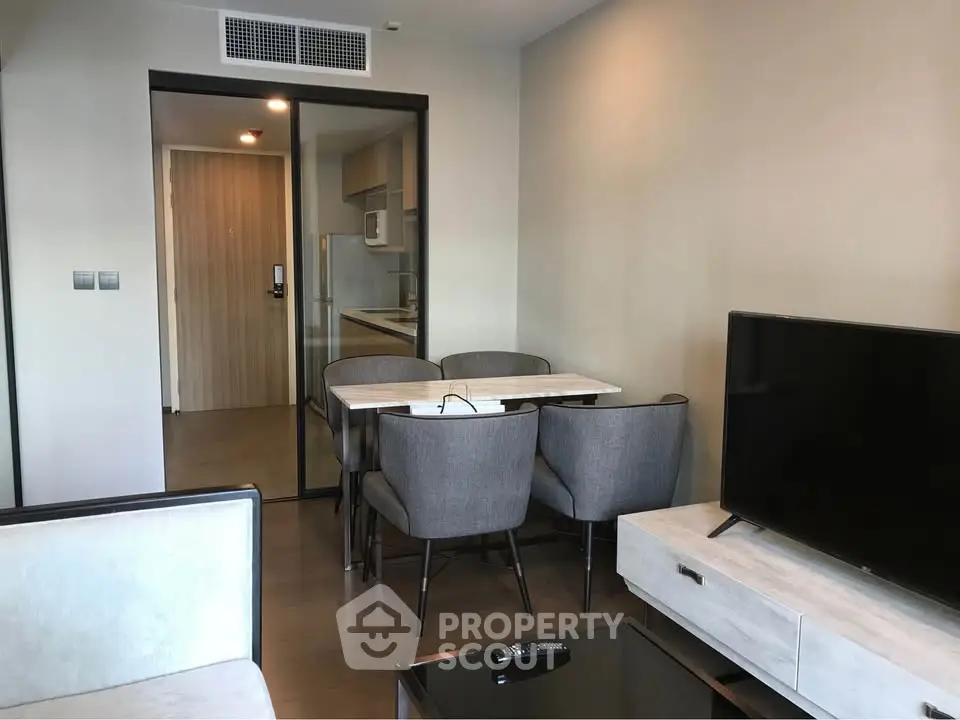 Modern living room with dining area and TV, featuring sleek furniture and open kitchen layout.