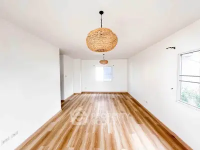 Spacious empty room with wooden flooring and stylish pendant lights.