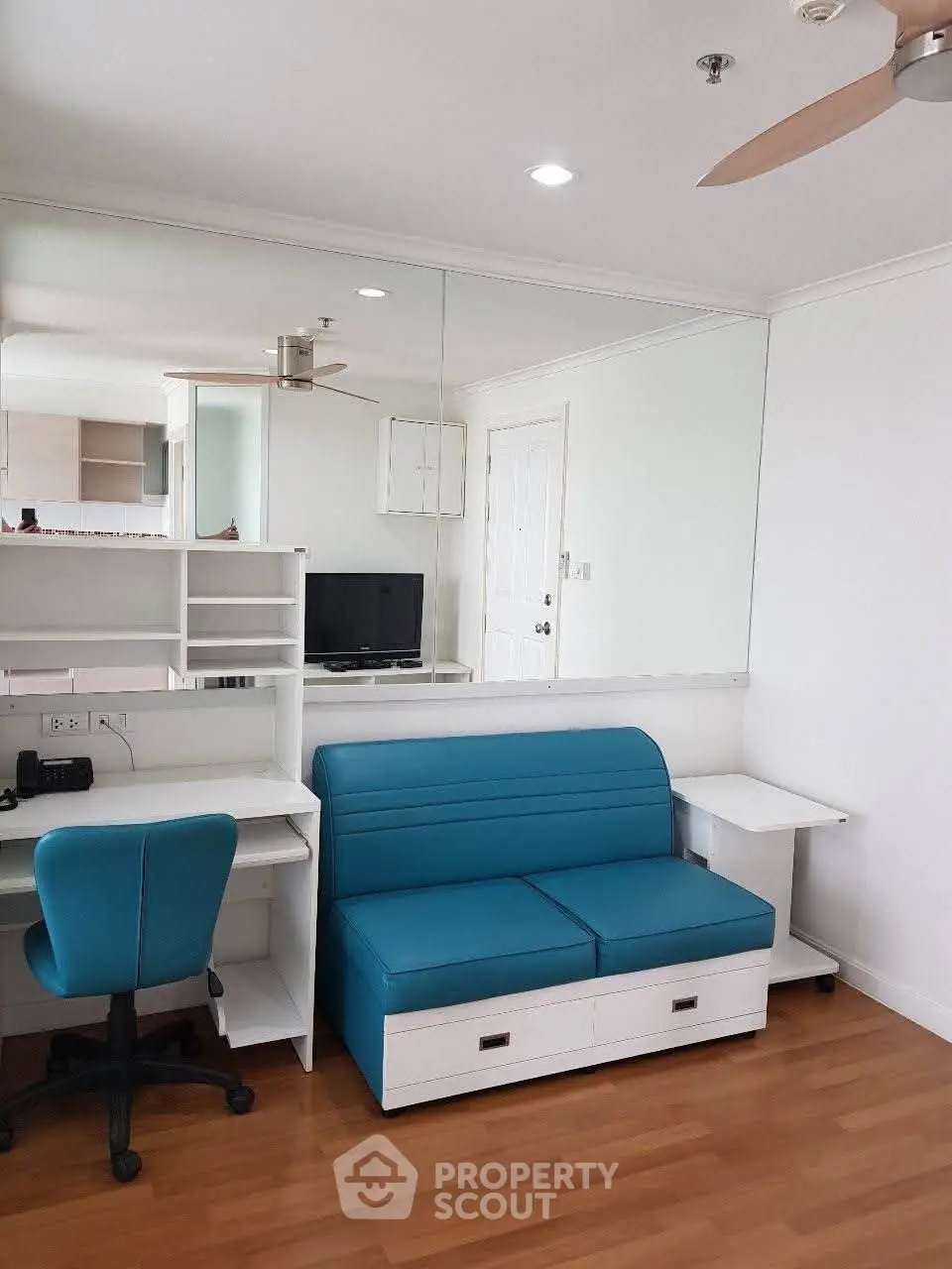 Modern living room with blue sofa, study desk, and mirrored wall in a stylish apartment.