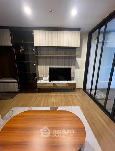 Modern living room with sleek wooden furniture and TV setup, featuring stylish shelving and glass partition.