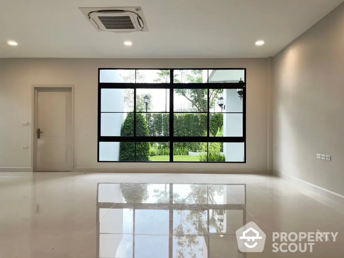 Spacious and modern living room with polished floors, large windows offering a serene garden view, and a sleek air conditioning unit.