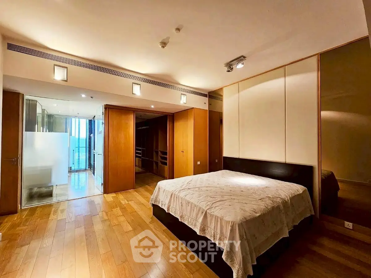 Spacious bedroom with wooden flooring and modern lighting in luxury apartment.