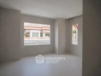 Spacious empty room with large windows offering natural light and view of neighboring houses.