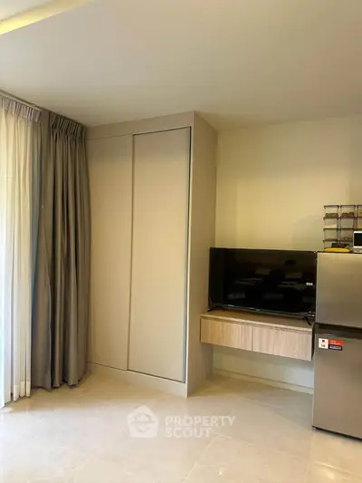 Modern living room with TV and fridge, featuring sleek design and natural light.