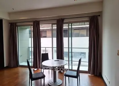 Modern living room with floor-to-ceiling windows and balcony access, featuring sleek furniture and hardwood floors.